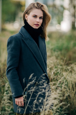Portrait of young blonde in gray coat on blurred background of green treesの写真素材