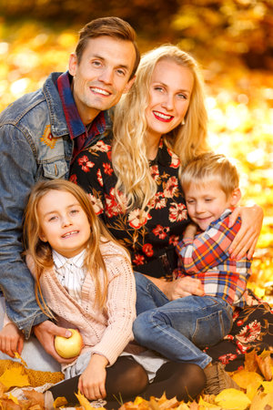 Close up photo of cheerful parents and children sitting in autumn parkの写真素材