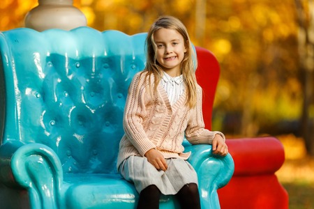 Image of girl sitting on blue chair in autumn park at afternoon.の写真素材
