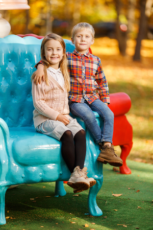 Photo of brother and sister sitting on blue chair in autumn parkの写真素材