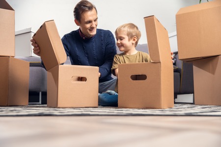 Photo of man and boy sitting on floor among cardboard boxesの写真素材