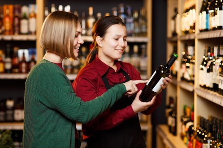 Image of two women with bottle of wine in store on background of shelvesの写真素材