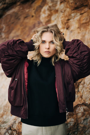 Photo of blonde with hands in her hair against stone wall in afternoon