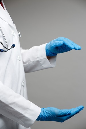 Photo on side of doctor in white coat with holding hands in form of circle isolated on gray background. Place for subject.の写真素材