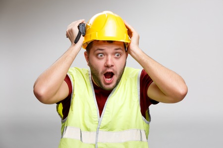 Photo of surprised builder in yellow helmet with walkie talkie on empty gray background.の写真素材