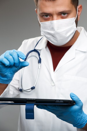 Image of doctor in mask and white coat in rubber gloves holding tablet.の写真素材