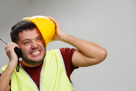 Photo of screaming builder in yellow helmet with walkie-talkie on empty gray background.の写真素材