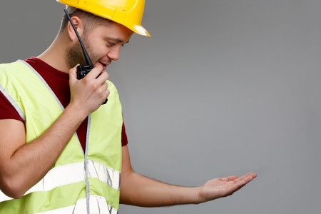 Photo of builder in helmet with walkie-talkie in his hand in yellow vest with raised palm up.の写真素材