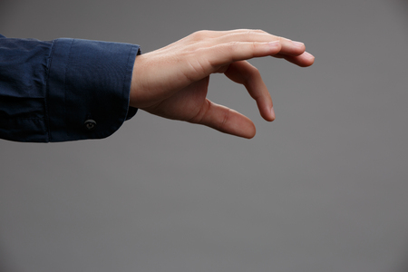 Photo of outstretched hand in blue shirt with palm down, holding something with two fingers on empty gray backgroundの写真素材