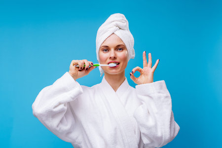 Picture of woman in white coat and towel on head brushing her teeth