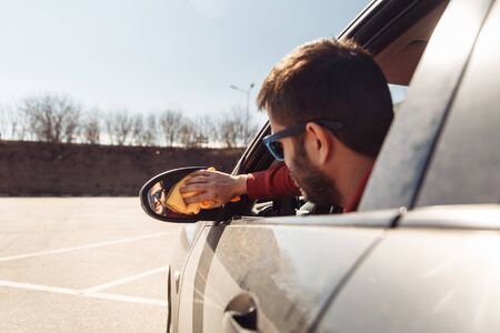 Image from back of man with orange rag washing distant-looking car mirrorの写真素材