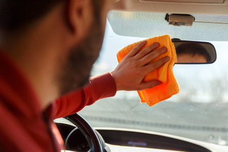 Image from back of man with orange rag washing mirror of car