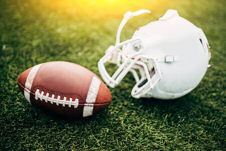 Image of white helmet of Amerinian football player and ball on green lawnの写真素材