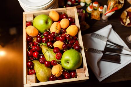 Image from above of wooden box with cherries, apples, apricots, pear on tableの写真素材