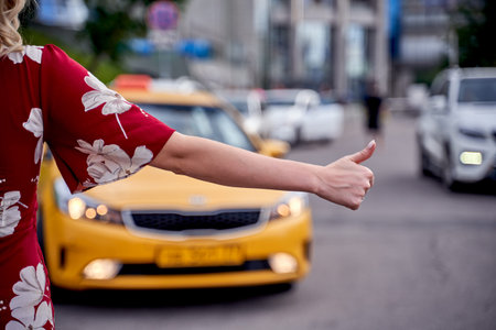 Picture from back of woman with outstretched hand stopping taxi in afternoon on blurred background .の写真素材