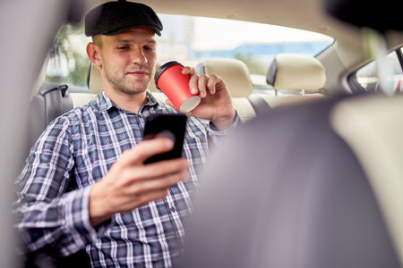 Photo of male passenger with phone in his hand sitting in back seat of car