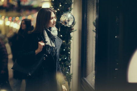 Photo side of young girl at shop window in evening
