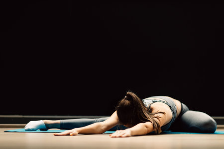 Athletic girl stretching lying on rug in sports hall