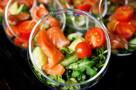 Close-up on top of buffet table with glass cups with salad of red fish, tomatoes, cucumber, herbsの写真素材