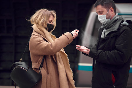 Brunet man and woman in medical masks using antiseptic while standing near underground carriage