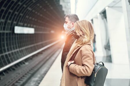 Side view of young man and woman in medical masks standing near carriage in subway. Coronavirus pandemic.の写真素材