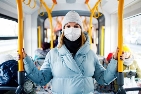 Masked young woman standing in bus lounge next to yellow handrails in afternoon.の写真素材