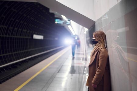 Bonde in black medical mask standing in subway near carriage.の写真素材
