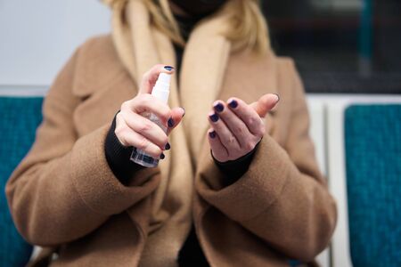Close up of woman in medical mask disinfects hands while sitting in carriage in subway.の写真素材