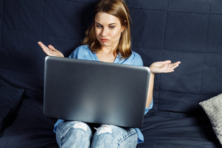 Smiling hipster girl talking with friends via an app on laptop, cheerful female student studying via...