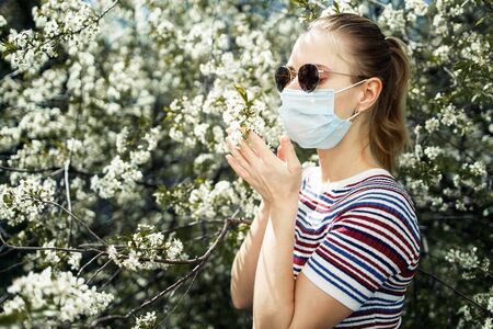 Side view of young girl in medical mask and sunglasses on background of blossoming apple tree on summer day.の写真素材