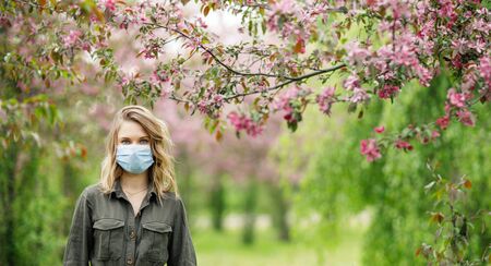 Young woman in medical mask on background of flowering trees in parkの写真素材