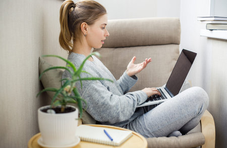 Side view of woman in gray home suit with laptop in her hands sitting in chair