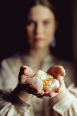 Young european girl holding a gemstone with boths hands in front of her. Looking towards the camera. Mystical woman. Occult, witchcraft scene.の写真素材