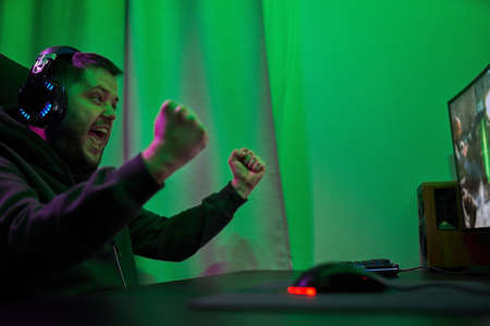Gamer or streamer in headphones with microphone sits at home in neon light and plays at pcの写真素材
