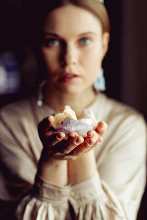 Young european girl holding a gemstone with boths hands in front of her. Mystical woman. Occult, witchcraft scene. Close up paranormal portrait.の写真素材