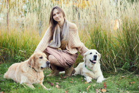 Beautiful girl with two golden retrievers in parkの写真素材