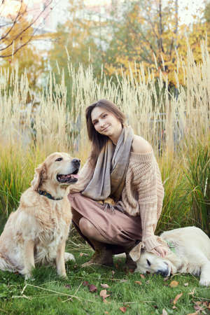 Beautiful girl with two golden retrievers in parkの写真素材
