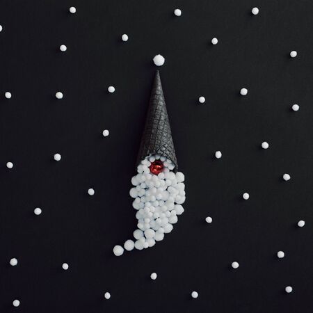 Christmas minimal concept - santa claus creative minimal on black background. Santa claus hat made of black ice cream cone and snowball. Stylish christmas creative minimal idea. Snowfall patternの写真素材