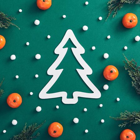 Christmas minimal concept - Christmas composition made of tree branch, snowfall and tangerine on dark green background. White Christmas tree shape. Xmas holiday concept. Snow winter pattern. の写真素材