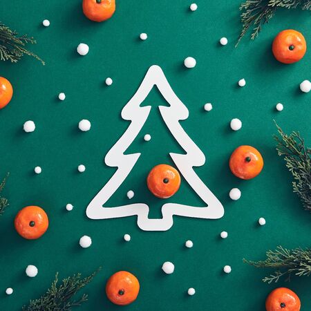Christmas minimal concept - Christmas composition made of tree branch, snowfall and tangerine on dark green background. White Christmas tree shape. Holiday christmas background. Holiday decoration.の写真素材