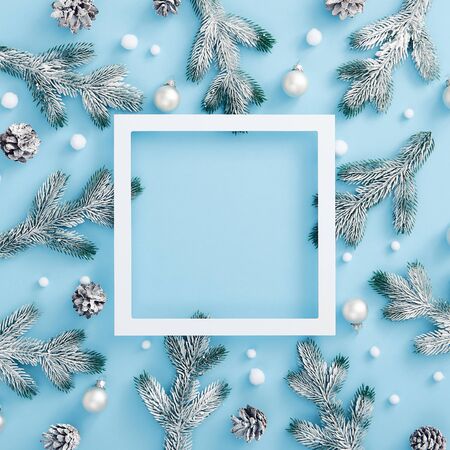 Christmas minimal concept - Christmas snowy decoration on pastel blue background. Pine branch and cone, bauble and abstract snowball. Square composition, flat lay. White paper frame with copy spaceの写真素材