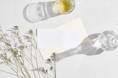 Realistic business card template on white background. Lifestyle mock up name card and envelope with empty place. Floral and sunny mockup. Paper blank for your design with floral elements and glassの写真素材