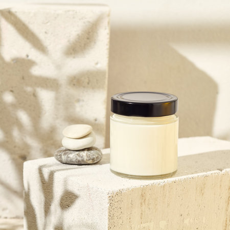 Glass jar for cosmetics on concrete podium. Mockup for natural cosmetics. Nature composition with beauty product in jar. Mockup soy wax candle in natural style. Empty jar with cosmetic productの写真素材