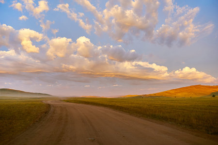 Clouds unusually highlighted by rising sun over dirt road