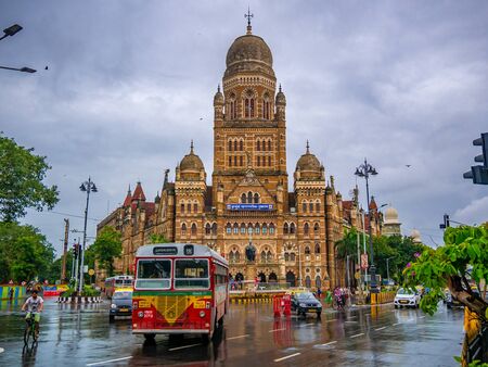 MUMBAI, INDIA - JUNE 24, 2018 : Best bus running across the street of BMC municipal building in Mumbai City, India. British architecture and historical building in Mumbaiのeditorial素材