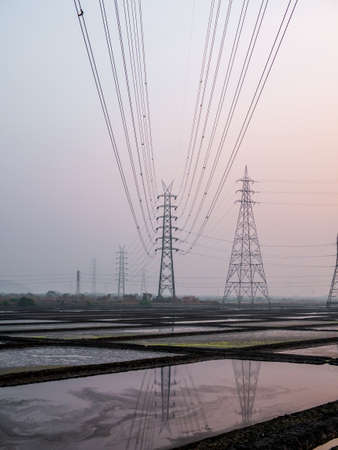 Reflection of High voltage power lines in Sea salt farm and barn at sunsetの写真素材