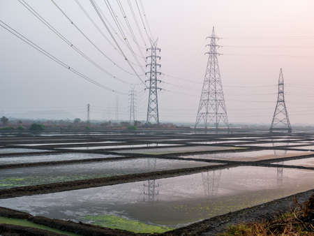 Reflection of High voltage power lines in Sea salt farm and barn at sunsetの写真素材
