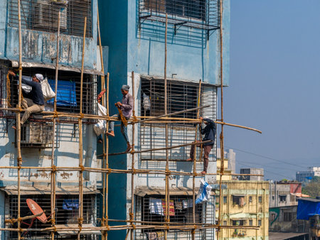 MUMBAI, INDIA - December 17, 2020 : Construction workers building a bamboo structure on a building wall to initiate the building maintenance. No protective gears.のeditorial素材