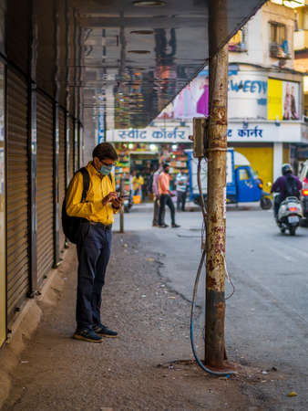 Thane, India, December 22,2020:Â  Indian man using a mobile covering his face with aÂ surgical mask to protect from Covid-19のeditorial素材