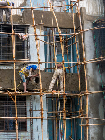 Mumbai, India - March 20, 2021 : Construction workers building a bamboo structure on a building wall to initiate the building maintenance. No protective gears.のeditorial素材